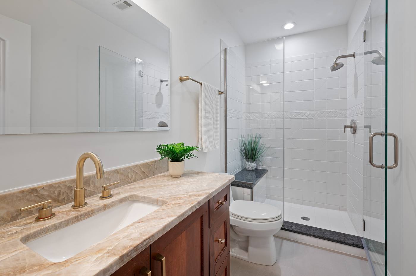 Lower-level full bath with quartzite counter, brass fittings and a glass shower