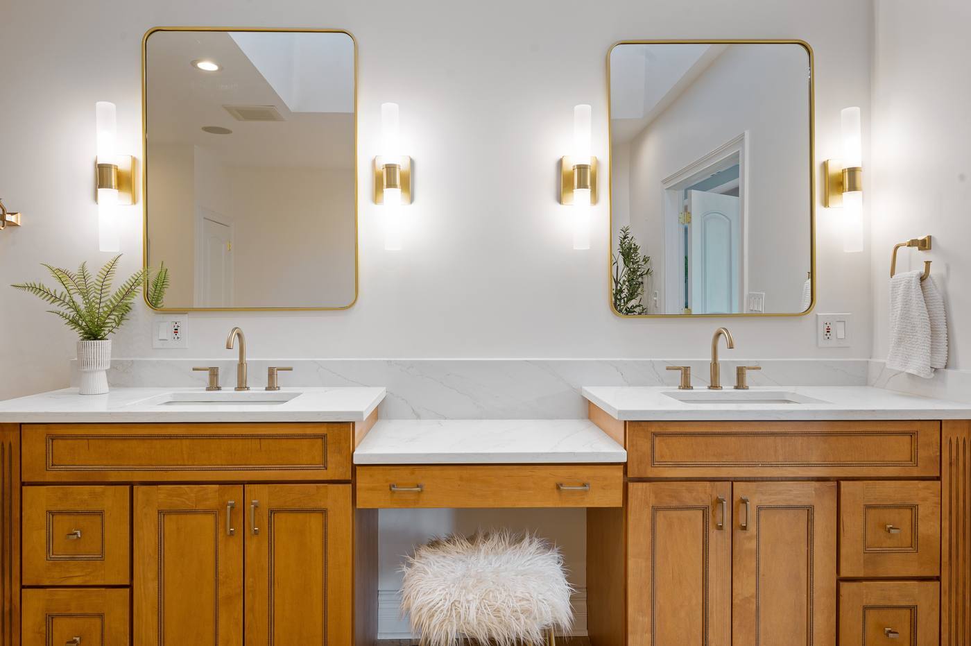 Primary bath double vanity with quartz counters, seated make-up station and brass sconces